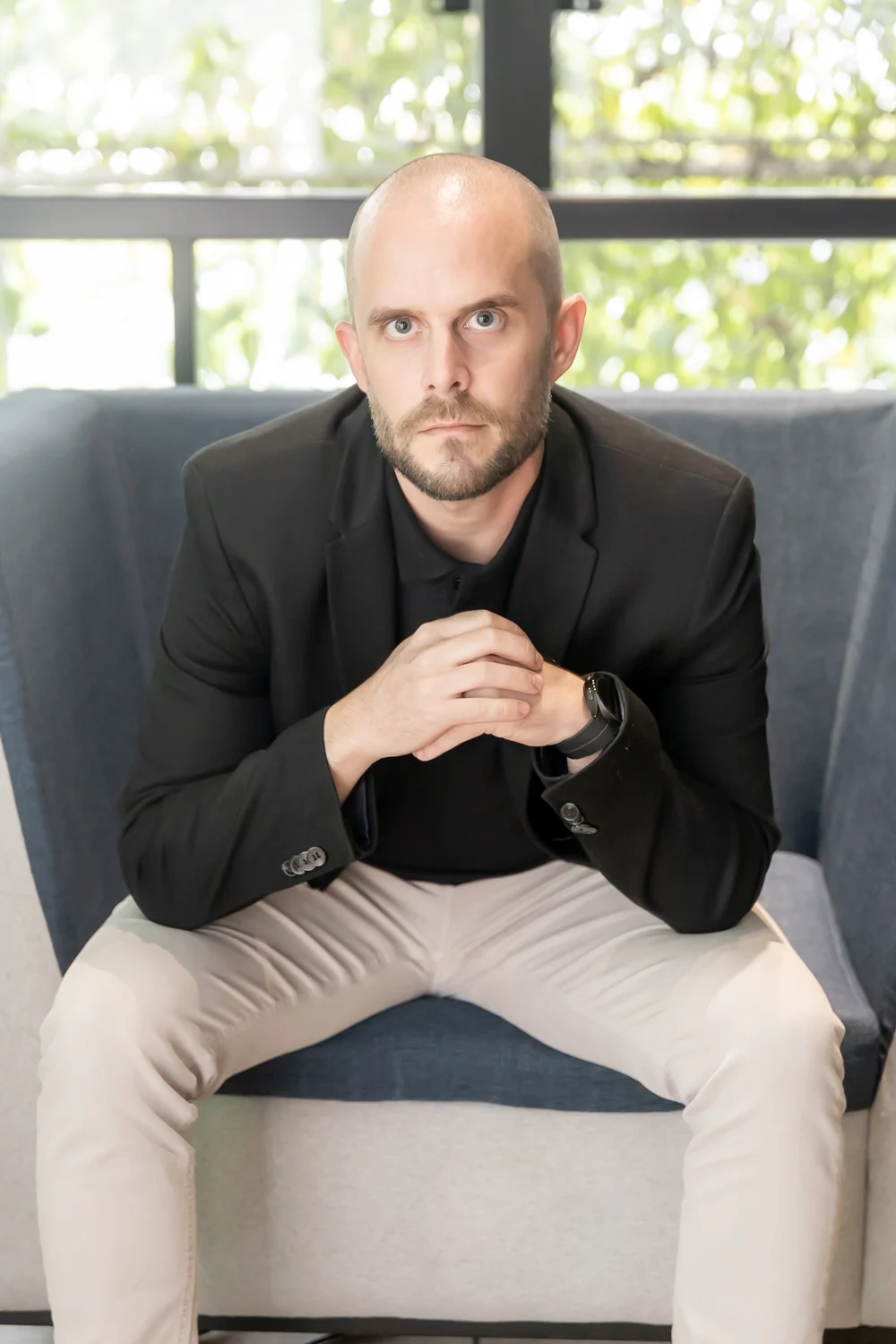 Dr. Guilherme Sanches, sentado num sofá azul, de blazer preto, olhando para a câmera